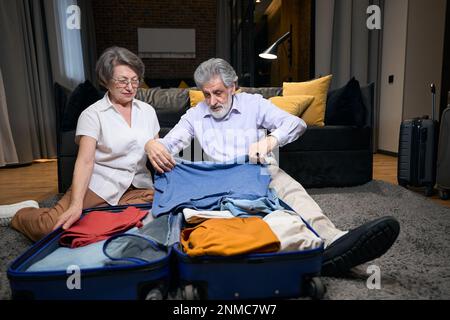 Old man folds clothes in trolley bag Stock Photo