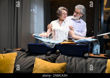 Old woman folds clothes in trolley bag Stock Photo