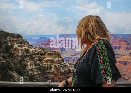 Woman with messy long hair leans on railing and looks out over Grand Canyon in USA Selective focus on woman Stock Photo