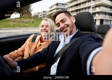 Happy middle-aged couple takes selfie in the car. Wife and husband pose and look smiling at camera. Stock Photo