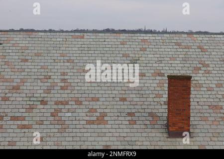 Slate roof of old building at Fort Adams State Park in Newport, Rhode Island.  Red chimney toward the right bottom. Tree tops poking out above roof. Stock Photo