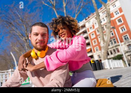Multiracial couple through the city streets, lifestyle, portrait embracing smiling sitting in a park Stock Photo