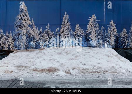 Privacy fence with photo of snow-covered fir trees, in front of it mountain with real snow, ice rink at the Koe, Duesseldorf, North Rhine-Westphalia Stock Photo