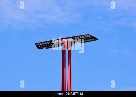 flat solar panel on top of red steel light pole or pylon. photovoltaic PV cells. low angle view. self sustained lighting. blue summer sky. Stock Photo