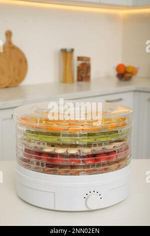 Dehydrator machine with different fruits and berries on white table in kitchen Stock Photo