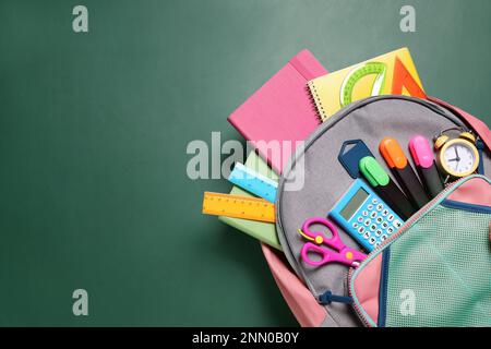 Backpack with different stationery on chalkboard background, top view. Space for text Stock Photo