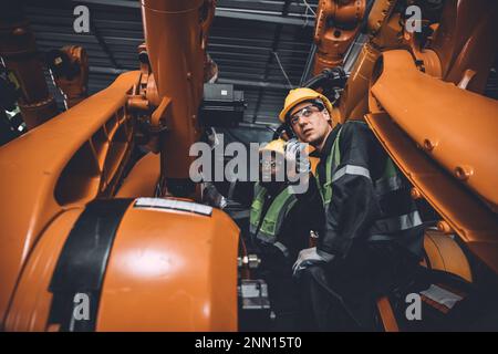 Engineer team service fix robot welding arm working in automation factory. People worker work in robotic arm assembly plant heavy metal industry. Stock Photo