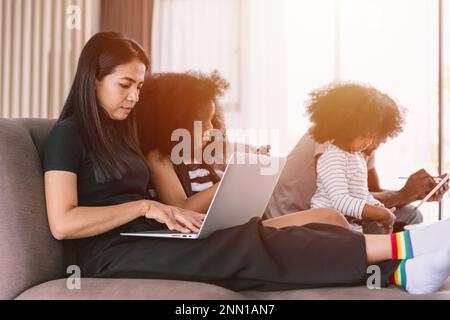 Business mom working woman busy mother holiday wireless work on laptop computer at home with daughter and family Stock Photo