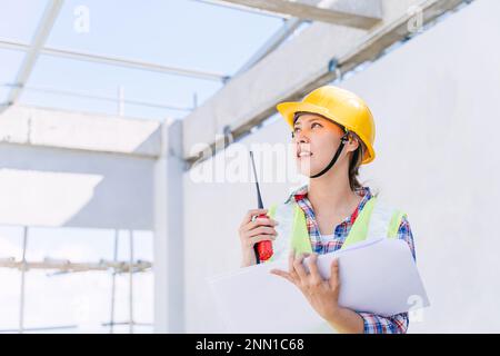 Asian woman engineer worker work in construction site. Smart builder architect female in safety suite working. Stock Photo
