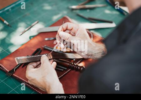 closeup hand working process leather handcraft in the leather workshop. Man holding crafting tool and working. He is sewing to make a walet. Tanner in Stock Photo