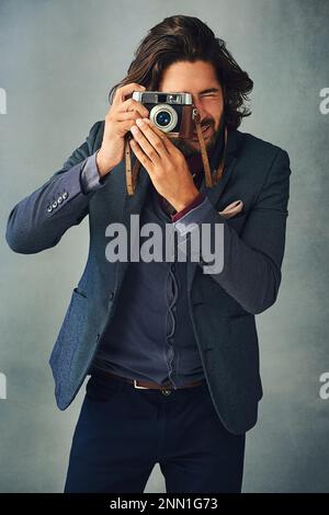 Hes and style and image maker. Studio shot of a stylishly dressed handsome young man taking a picture with a vintage camera. Stock Photo