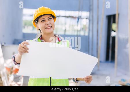 Asian woman engineer worker work in construction site. Smart builder architect female in safety suite working. Stock Photo