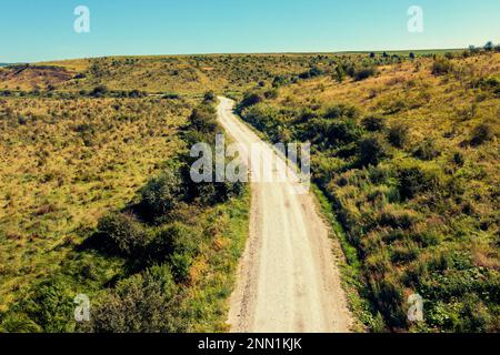 Drone view of the dirt road between hills on a sunny summer day Stock Photo