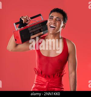 Happy, man and boombox radio in studio for gay, pride and vogue aesthetic with retro 80s tech by red background. Lgbtq model, vintage fashion and Stock Photo