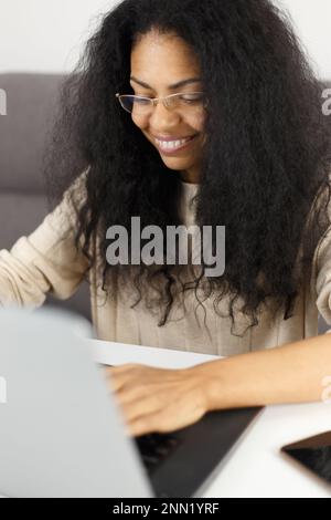 Happy black woman in glasses working on computer at home. Successful POC entrepreneur using a laptop for business Stock Photo