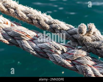 Two weathered hemp ropes for fastening ships in a harbour. Greenisch sea water surface in the background Stock Photo