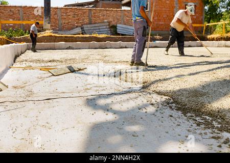 Construction workers, masons are using rake to spreading, leveling concrete covering square trench, pouring layer of concrete in foundation. Stock Photo