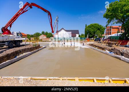 Construction site, mixer truck for pouring fresh concrete into pump, machine pumping to exit tube, building foundation, riggers, workers are leveling Stock Photo