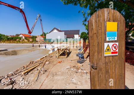 Open door made of wooden planks with warning signs on it, site entrance, foundation of residential building is under construction in background. Stock Photo