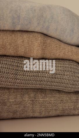 knitted warm pastel color sweaters with different knitting patterns folded in stack, Close up, copy space for text. Stock Photo