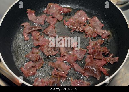 Slices and pieces of pastrami that is being roasted by heat with ghee and oil in a cuisine that scrambled eggs will be added and to prepare fried egg Stock Photo