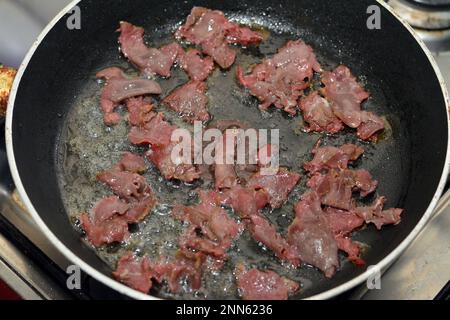 Slices and pieces of pastrami that is being roasted by heat with ghee and oil in a cuisine that scrambled eggs will be added and to prepare fried egg Stock Photo