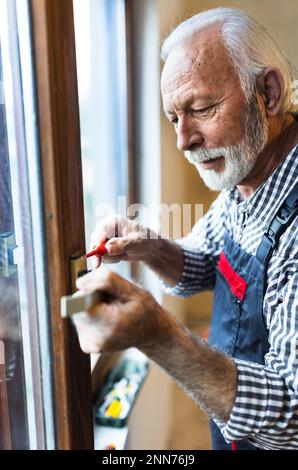 Senior man worker repairing window handle with manual screwdriver in home renovation process Stock Photo