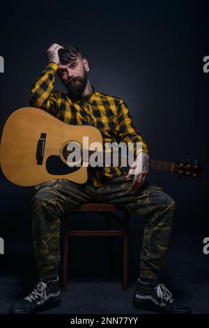 Man with tattoos and beard is hoding a guitar and is wearing a tartan yellow black shirt Stock Photo