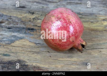A closeup of a ripe pomegranate on a rustic wooden table Stock Photo
