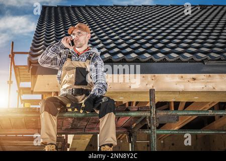 Caucasian Contractor Talking on the Phone While Sitting on Scaffolding at the Construction Site. Industrial Workers Theme. Stock Photo