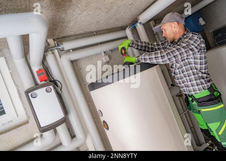 Professional Caucasian Plumber Fixing Residential Heating System Boiler Using Screwdriver. Stock Photo