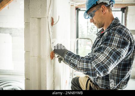 Professional Electrician in Safety Equipment Installing Electrical Wiring System in Freshly Built Residential House. Stock Photo