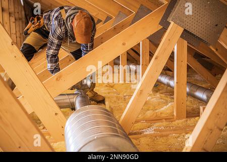 Professional HVAC Technician Installing Air Ducts in the Wooden Roof Section of the Building. Ventilation Systems Theme. Stock Photo