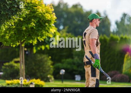 Smiling Caucasian Gardener with Hedge Shears in His Hand During Pruning and Trimming Work in Residential Backyard Garden. Stock Photo