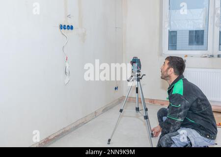 Man makes repairs in new apartment. Builder levels walls using laser level. High quality photo Stock Photo