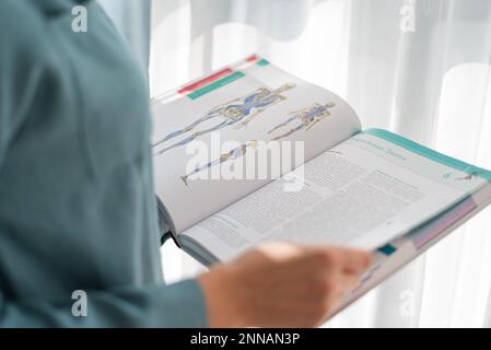 blonde doctor girl holds an encyclopedia with the image of a human skeleton in her hands. medicine, student, exams, training, experience, publisher, w Stock Photo