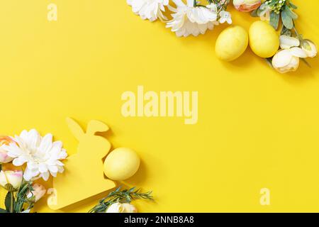 Easter composition with colorful eggs, wooden bunny and spring flowers on yellow background. View from above. Copy space. Stock Photo