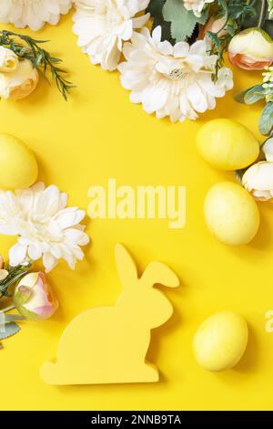 Easter composition with colorful eggs, wooden bunny and spring flowers on yellow background. View from above. Stock Photo