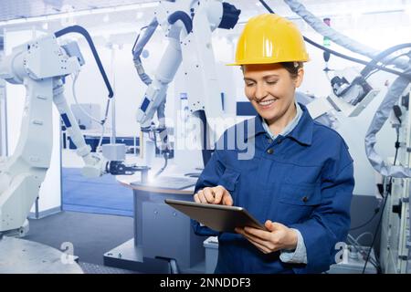 Woman engineer uses a digital tablet to control robots in a smart factory. Smart industry 4.0 concept Stock Photo