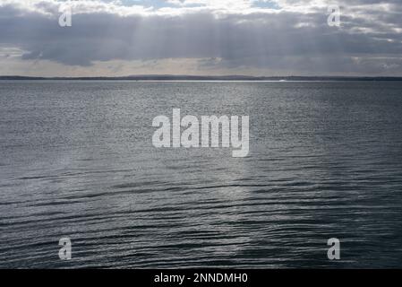 Sun rays breaking through clouds across an empty ocean with land in the distance. The emptiness giving the feeling of peace, calm and being alone Stock Photo