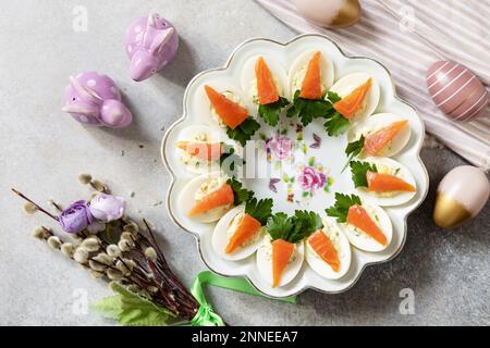 Festive dinner, Easter brunch. Stuffed eggs with cheese and salted salmon in the form of a carrot. View from above. Stock Photo