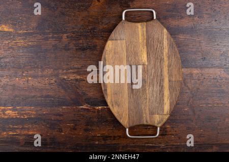Wooden cutting board, oval, vintage, with iron handles on a wooden background. View from above Stock Photo