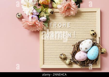 Letter board, Frohe Ostern - Happy Easter in german greeting, Easter eggs and spring flowers on a pastel pink background. View from above. Stock Photo