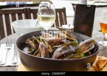 Bowl of New Zealand green lipped mussels on table with wine in open air restaurant in Akaroa, New Zealand. Stock Photo