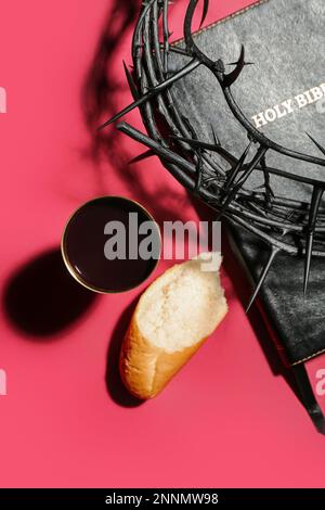 Crown of thorns, Holy Bible, cup of wine and bread on red background Stock Photo