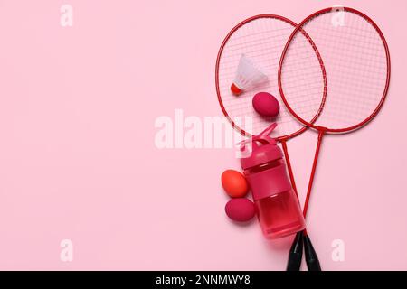 Badminton rackets, shuttlecock, water bottle and Easter eggs on pink background Stock Photo