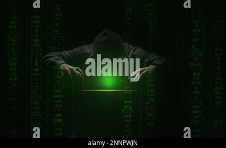 hacker over a screen with green binary code. Crime and Information Theft and Computers Stock Photo