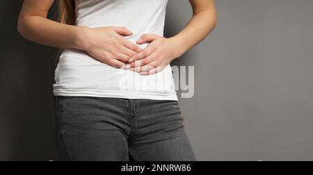 midsection of unrecognizable young woman holding her stomach with both hands - concept for dysmenorrhea, abdominal pain, irritable bowel syndrome Stock Photo