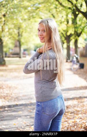 teenage girl enjoying sunny day in park - rear view of young woman wearing jeans and sweater turning head around Stock Photo