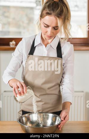 young woman pouring flour from glass mixing stainless steel bowl Stock Photo